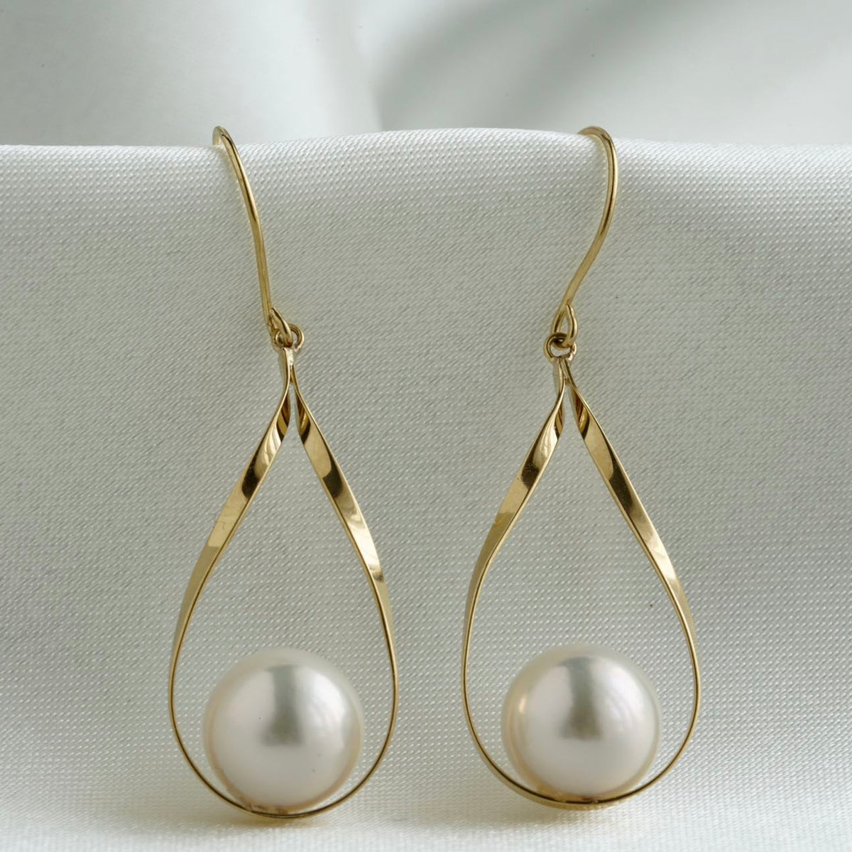 Pair of gold teardrop earrings with white Akoya pearls on a white fabric background